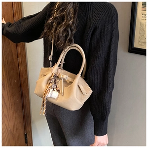 Close-up of beige lychee leather bag with coffee tassel charm and decorative metal buckle