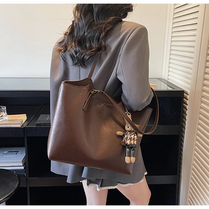Detail view of the deep brown leather tote bag featuring a cute teddy bear charm