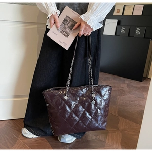 Detail of burgundy quilted patent leather tote bag with silver chain and metal charm