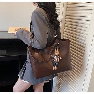 Detail of dark brown leather tote bag with plush rabbit charm worn by a model