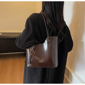 Detail of a shiny chocolate bucket bag with rope charm carried by a model from the side
