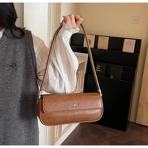 Close-up of brown vintage leather baguette bag with silver metal logo on a model
