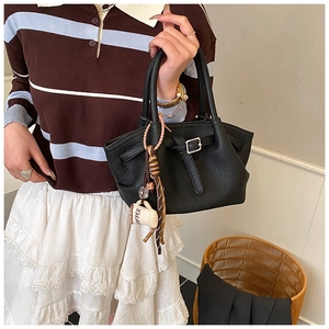 Detail of black lychee grain leather bucket bag with metal buckle and coffee charm