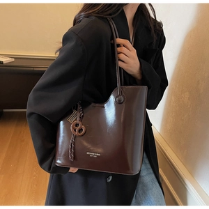 Detail of dark brown glossy leather tote bag with embossed brand logo and round charm