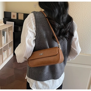 Detail of a brown leather shoulder baguette bag with metallic logo and sleek strap