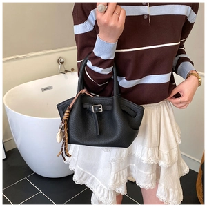 Detail of black lychee grain leather handbag with braided fringe and metal buckle hardware