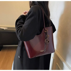 Detail of burgundy tote bag showing gold logo lettering and woven strap ornament