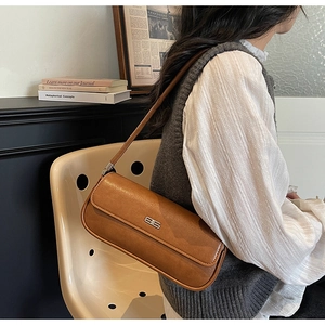 Close-up of caramel brown leather baguette bag with silver buckle and narrow shoulder strap