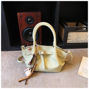 Detailed view of light green leather wing bag with coffee charm and pebble texture