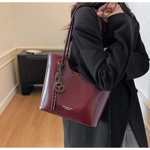Close-up of wine red glossy leather tote bag featuring woven rope and round charm details