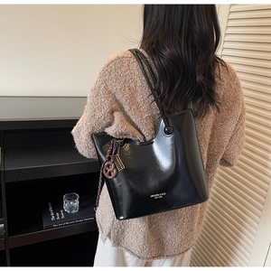 Detail of black glossy tote bag with pretzel charm shown in a minimalist home setting