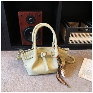 Close-up of light green lychee texture leather bucket bag with boho tassel detail