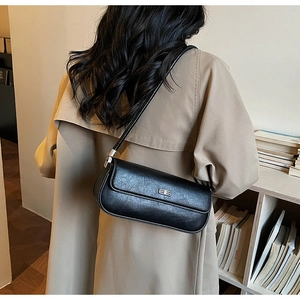 Detail showing a black leather baguette bag with a metallic BB logo worn over the shoulder
