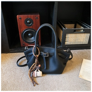 Detail of black pebbled leather bucket bag with coffee cup charm on gray carpet