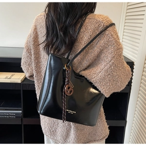 Detail of minimalist black glossy tote bag with brand logo and braided charm on a shoulder strap