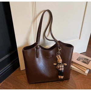 Close-up of brown faux leather tote bag with fashion text and rabbit charm on wood floor