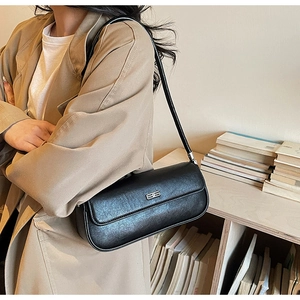 Detail of black minimalist baguette bag with silver metal logo and slim shoulder strap
