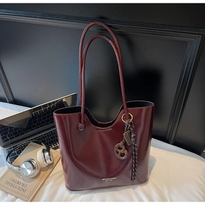 Detail of burgundy glossy tote bag with brand lettering and metal abacus charm