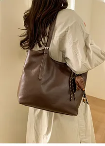 Detail of dark brown leather tote bag with adjustable metal buckle and woven tassel charm