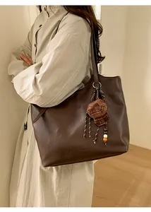Detail of dark brown leather tote bag with unique plaid cap charm and fringe tassel