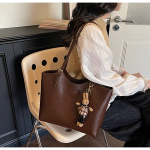 Detail of brown leather tote bag with rabbit charm decoration on a vintage chair