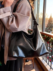 Sac hobo minimaliste en similicuir verni noir brillant porté par un mannequin chic
