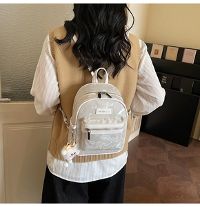 Detailansicht eines kleinen weißen Rucksacks mit Perlmutt-Textur und Plüschanhänger am Model