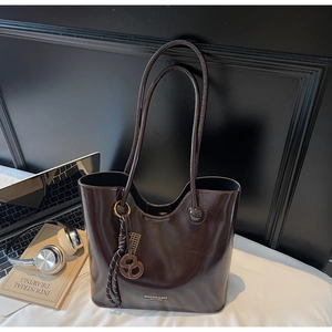 Detail of dark brown tote bag with glossy leather texture and metal abacus charm