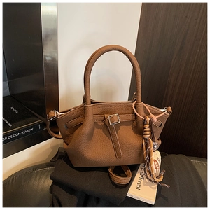 Close-up of brown pebbled leather bucket bag with silver buckle and tassel charm detail