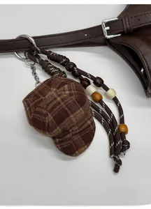 Close-up of a brown plaid hat charm with woven ropes and beads on a tote bag