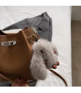 Close-up of a grey plush bunny charm attached to a brown leather bucket handbag