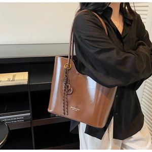 Detail of brown glossy leather tote bag with gold branding and a woven B charm