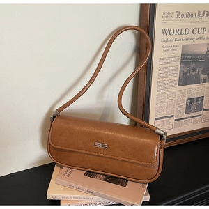 Detailed view of brown leather baguette bag with silver metallic logo on art books