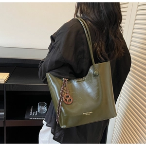 Detail view of the deep olive green leather tote bag featuring branded logo and charm