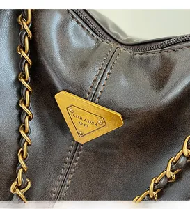 Macro detail of dark brown leather texture with a vintage gold metal logo and chain strap