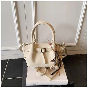 Detail of cream white leather bucket bag with tassel and plush coffee cup charm on books