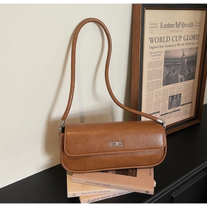 Close-up of brown leather baguette bag with silver logo on vintage books
