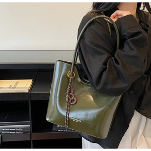 Detail of dark green leather tote bag with logo and brown woven charm accessory