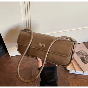 Detail of dark brown leather baguette bag with metal B-shaped buckle on white door background