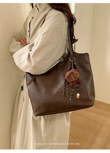 Minimalist large brown tote bag with decorative pendant shown on a shoulder