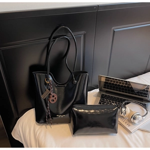 Detail of glossy black leather tote bag with matching pouch and golden branding accents
