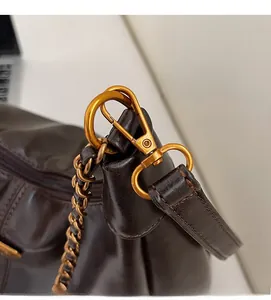 Close-up of golden metal lobster clasp and chain on dark brown leather dumpling bag