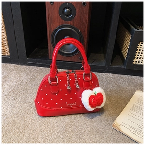 Close-up of red polka dot shell bag featuring Helahe logo and plush apple pendant