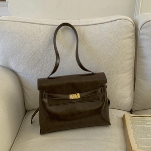 Detailed view of dark brown leather tote with a gold twist-lock on a cozy sofa