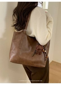 Detail of a large vintage brown leather tote bag with adjustable strap and charm on a model