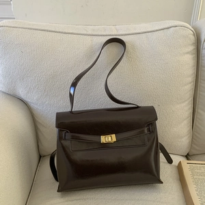 Detailed close-up of dark brown patent leather handbag with golden twist-lock on a sofa
