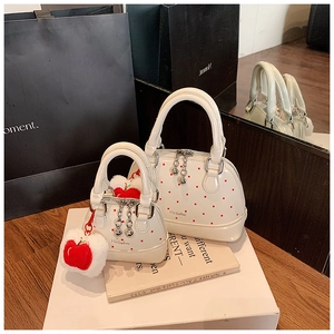 Detail of cream patent leather shell bag with red polka dots and apple plush charm