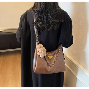 Brown leather hobo bag featuring gold triangle hardware and a cute plush bear charm