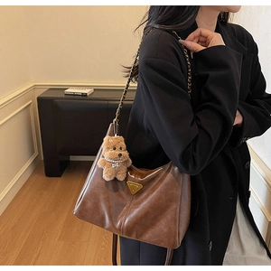 Detail of vintage brown tote bag with gold logo, chain strap and cute bear charm