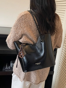 Glossy black leather tote bag with stylish pendants shown on a model in a modern setting